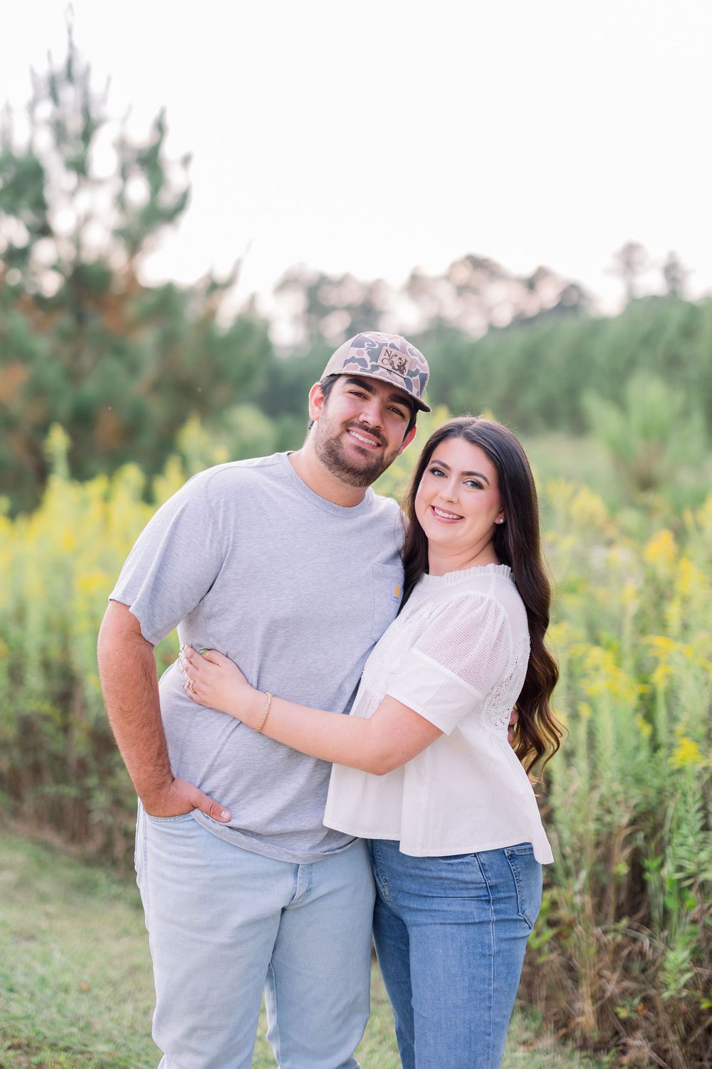 A casual couple posing together in a field of wildflowers and pine trees.