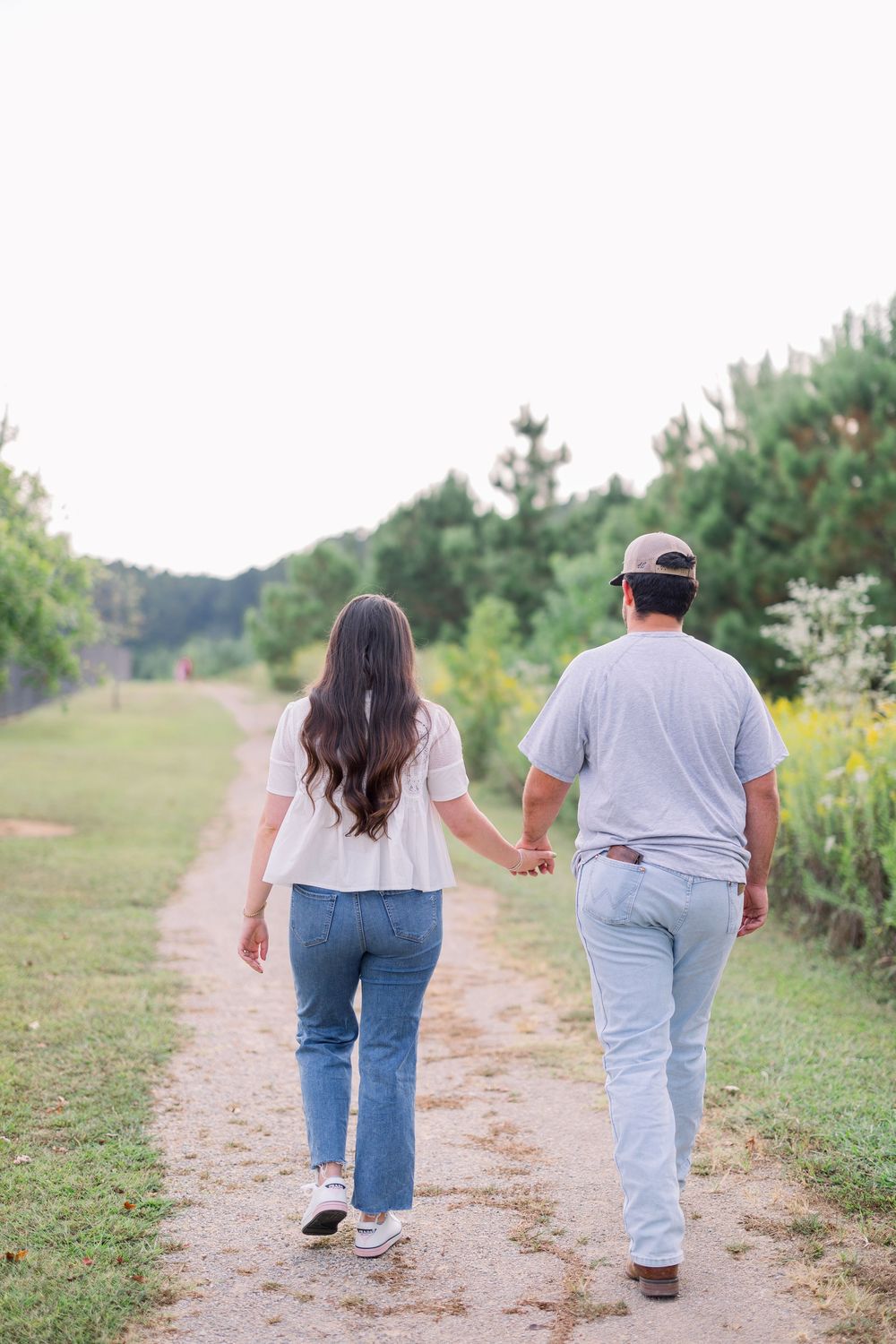 A couple walking hand in hand down a nature trail surrounded by greenery.