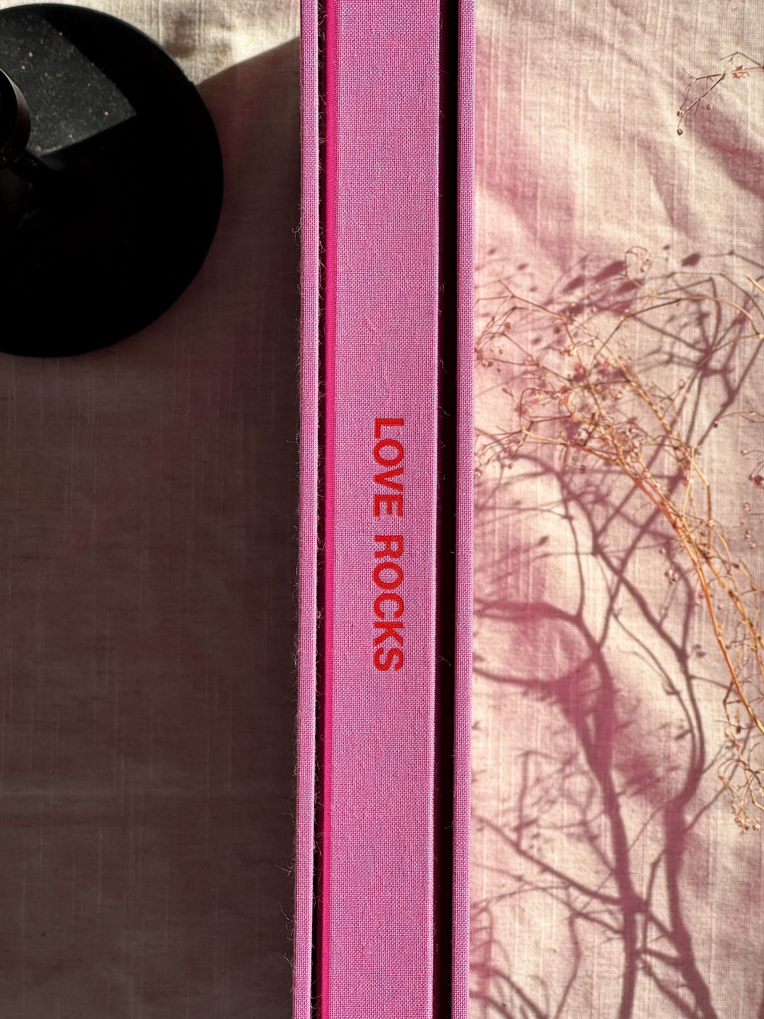 A series of pink book spines arranged in a row against a light background with shadows creating an artistic pattern.