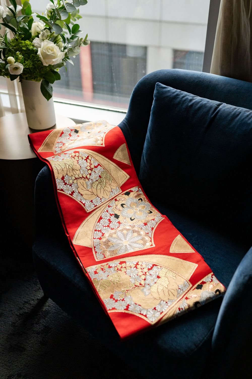 Traditional red and gold Chinese wedding decorations arranged on a navy blue couch near a window.
