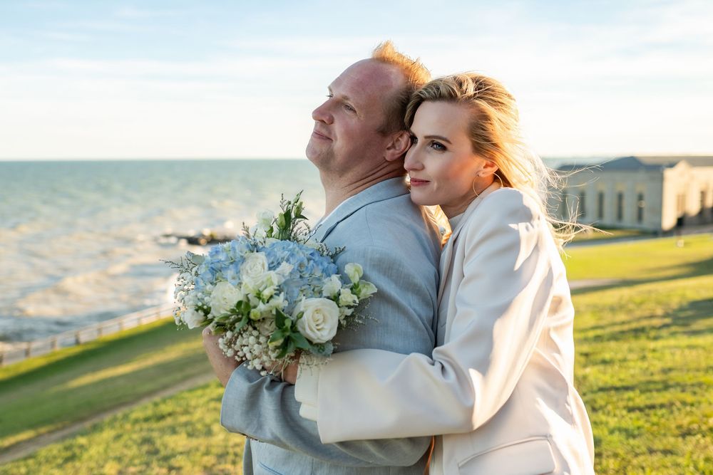 Romantic couple embraces in a sunlit meadow during golden hour while wearing light colored wedding attire.