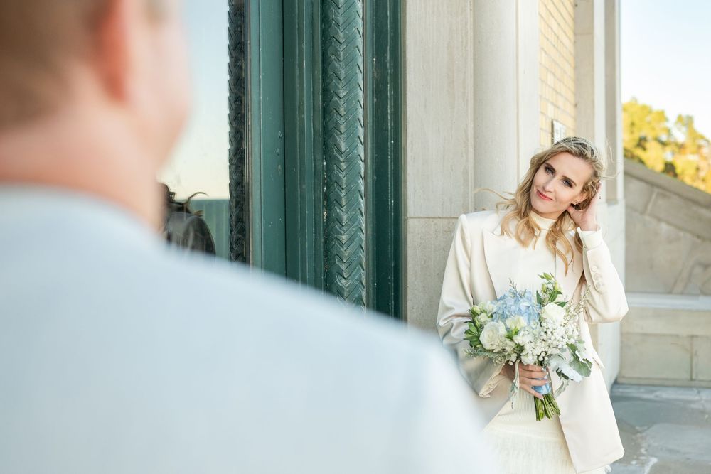 A couple in formal wedding attire poses together on marble steps with elegant architectural details.
