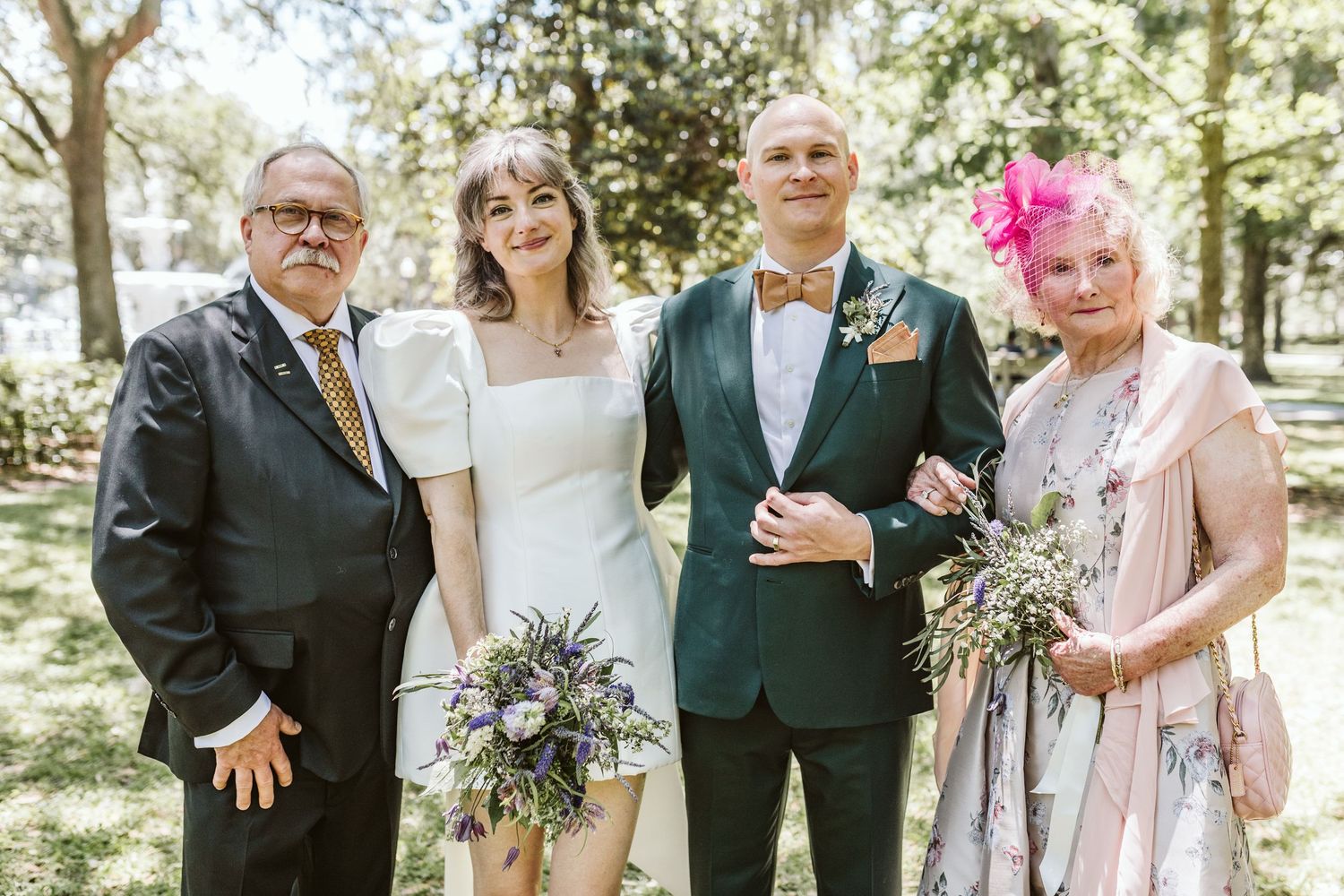 Wedding party members pose together in a sunny outdoor garden setting.
