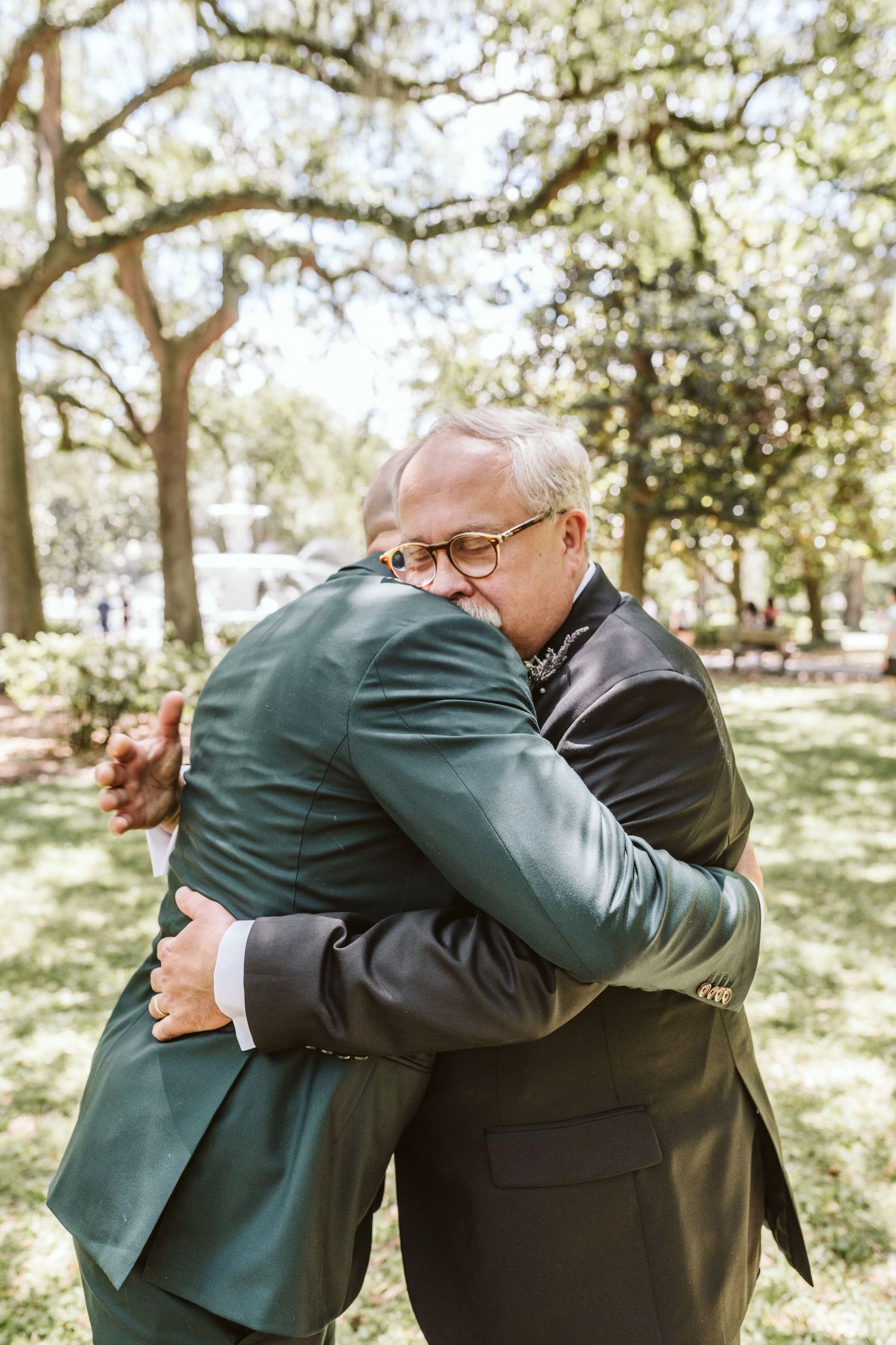 Two people share emotional embrace outdoors during wedding celebration.