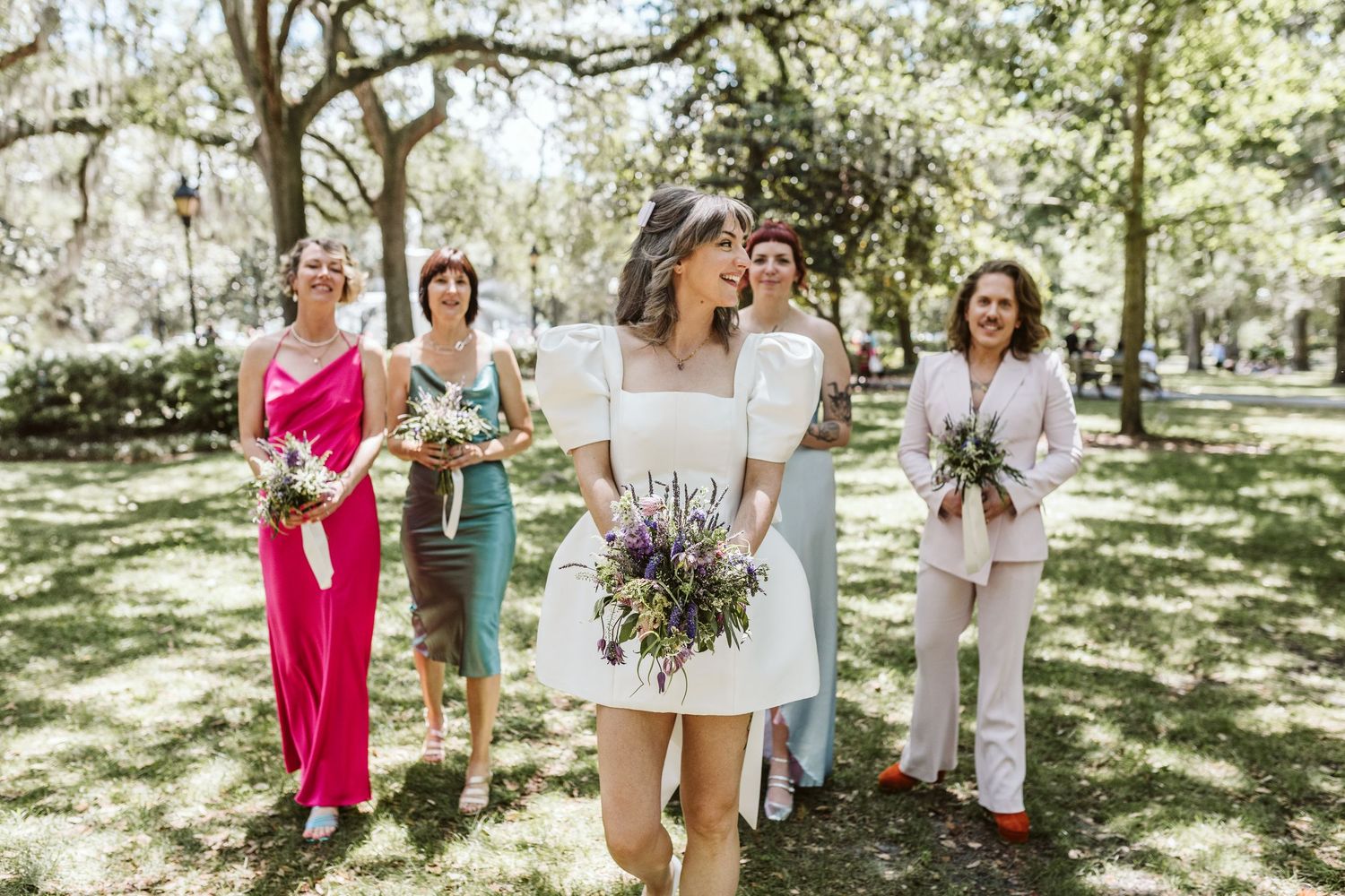 Wedding party members gather for casual outdoor photos in a sunlit garden setting.