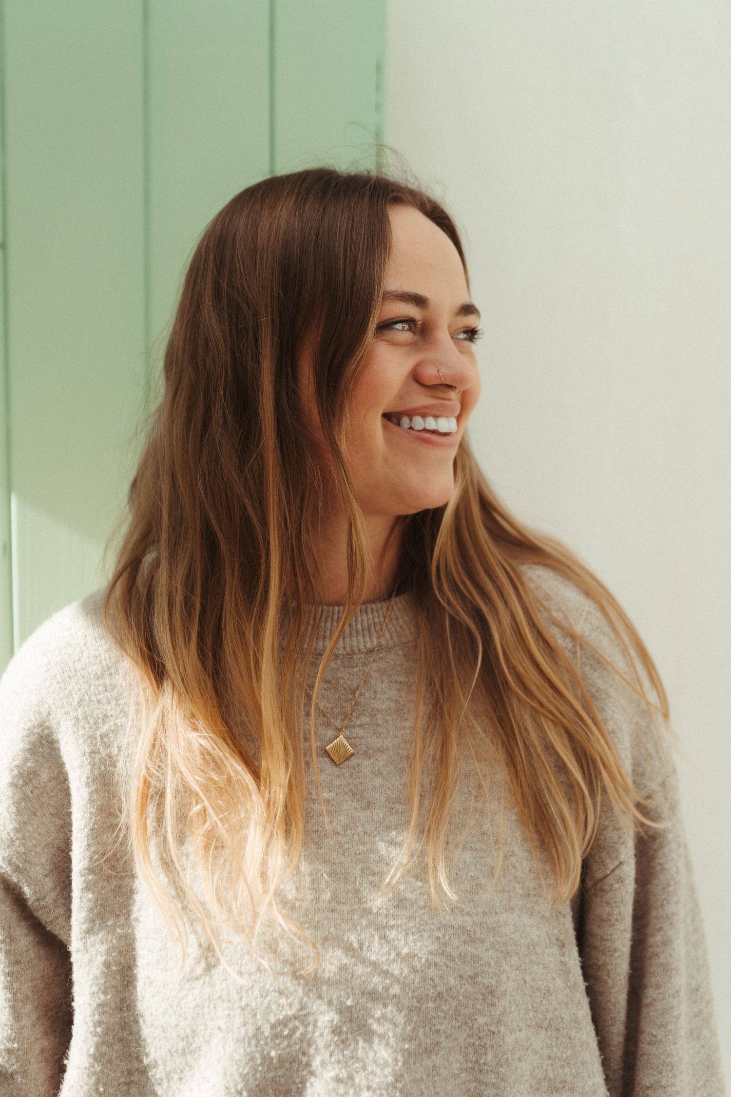 A series of four photos showing a person in a beige sweater with long brown hair laughing against a mint green background.