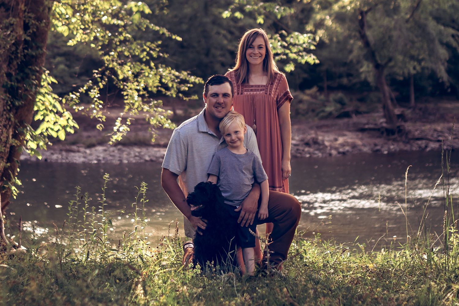 Family photo session in a sunlit wooded area near a stream.