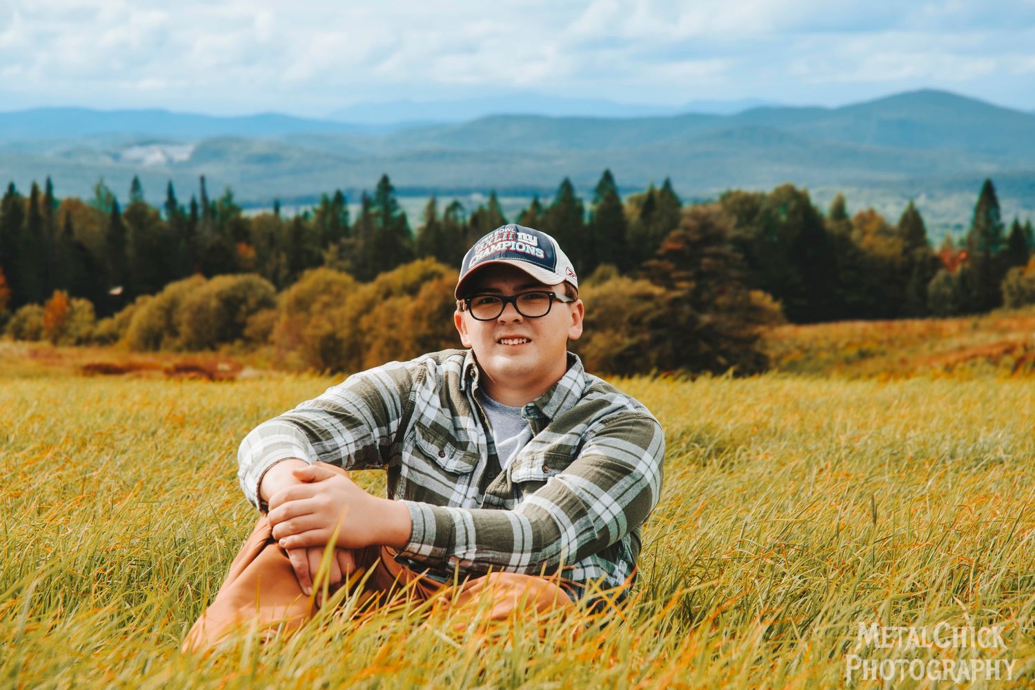 Senior portrait by Northern Exposure featuring a high school senior sitting in a field with mountains in the background