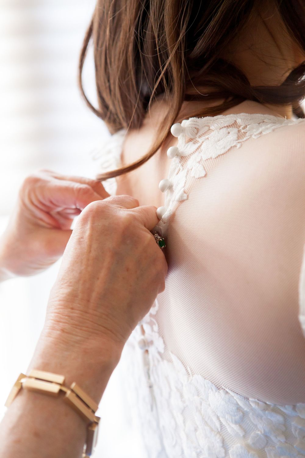 Close-up detail of lace appliques being adjusted on a white wedding dress.