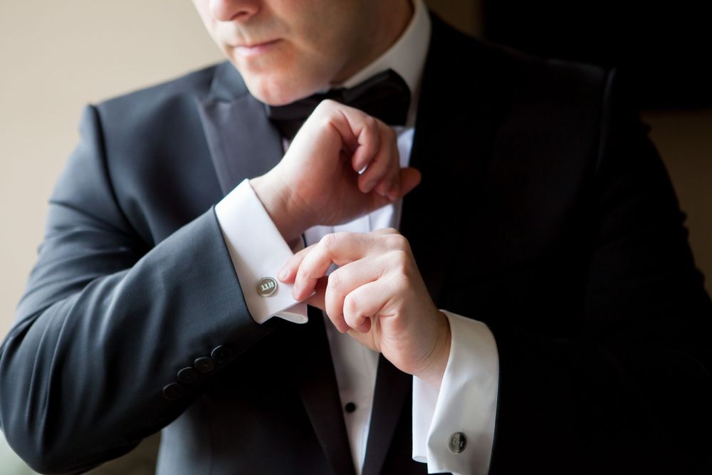 Formal black tuxedo and white dress shirt being adjusted during wedding preparation.