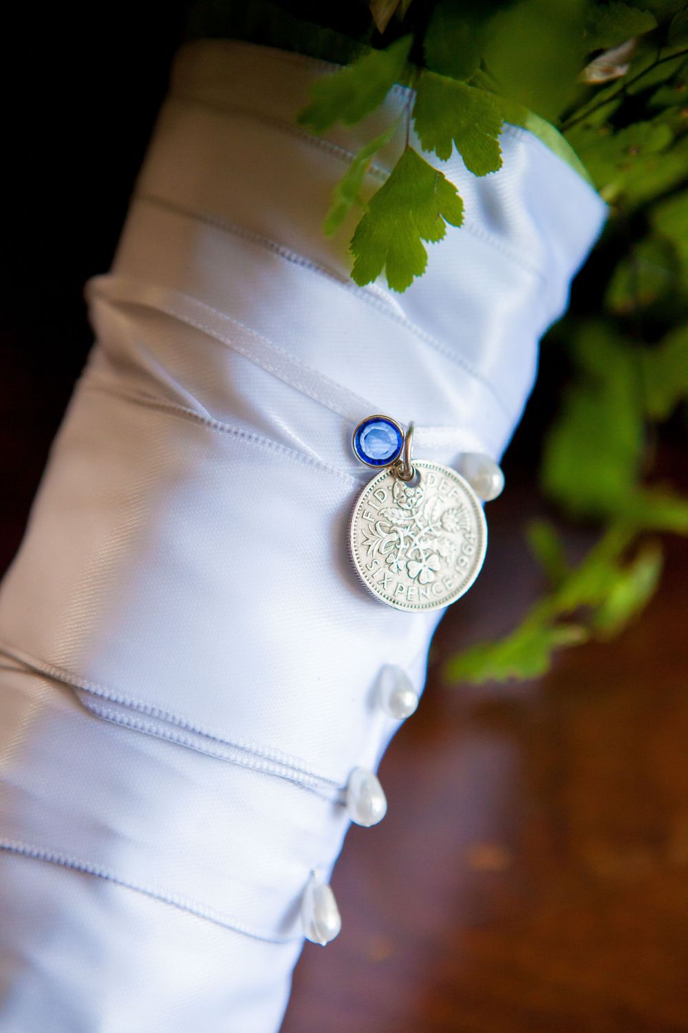 Close-up of a white shirt cuff with a vintage sixpence coin charm attached to a blue ribbon.