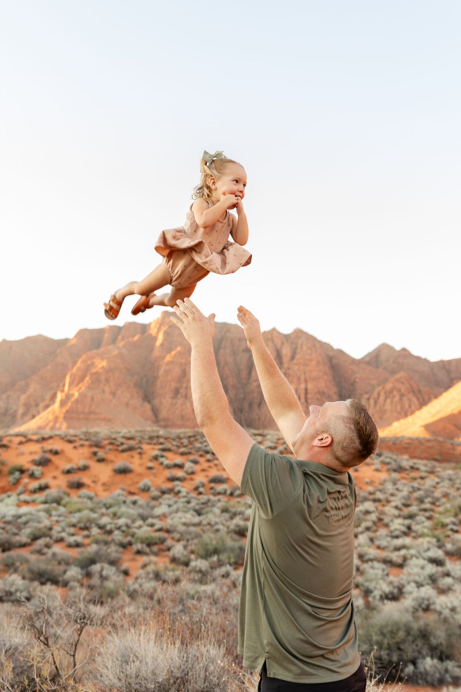 dad throwing 2 year old up in the air. red mountains and blue skies in the background