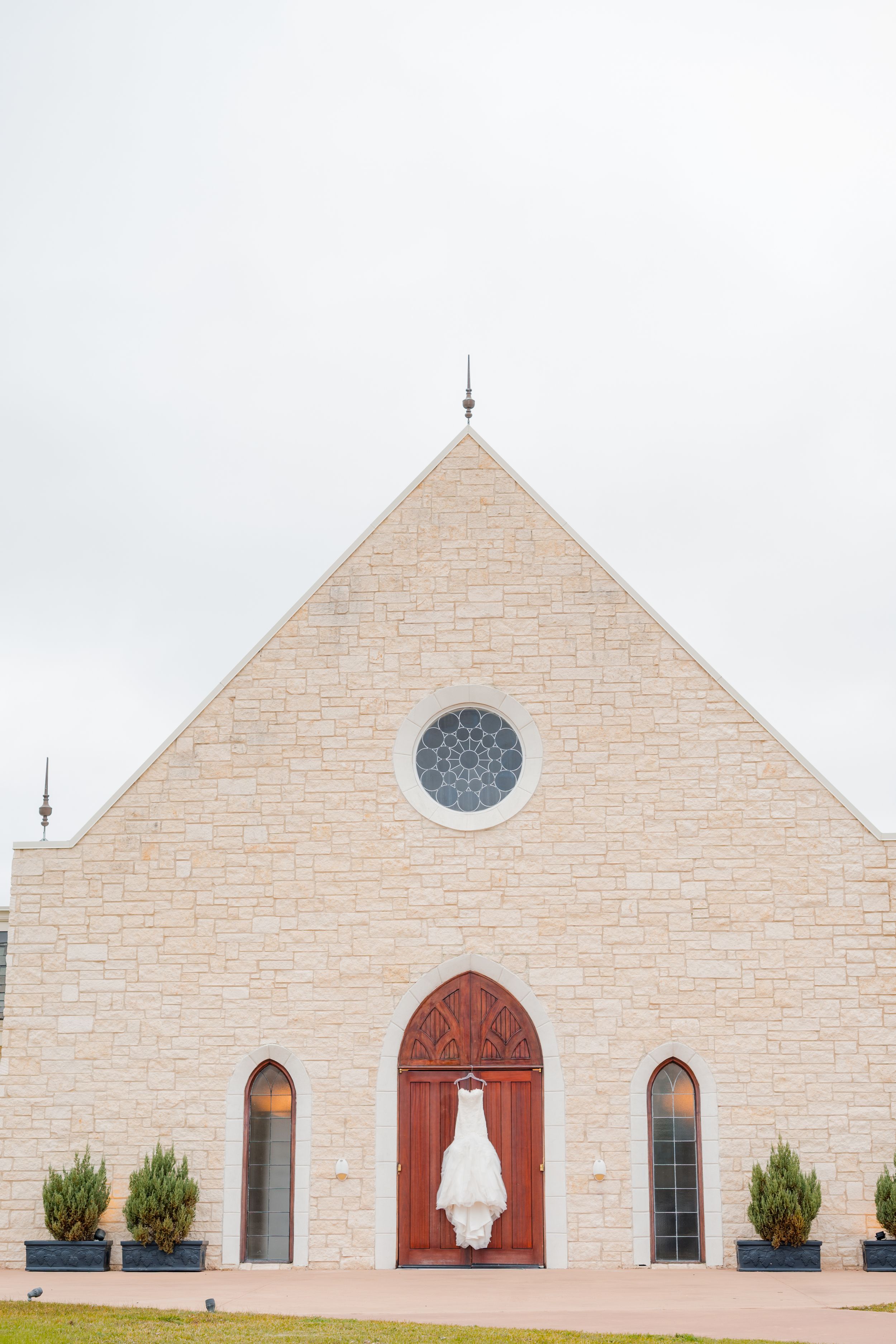 Modern church exterior with cream-colored stone walls, arched windows, and red wooden doors in a minimalist design style.