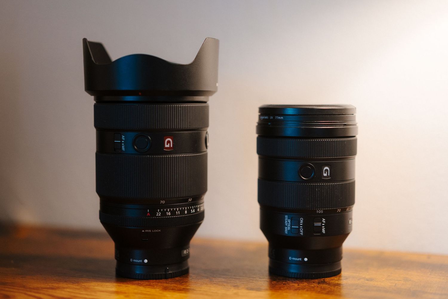 Multiple black camera lenses lined up on a wooden surface showing size comparison and different focal lengths.