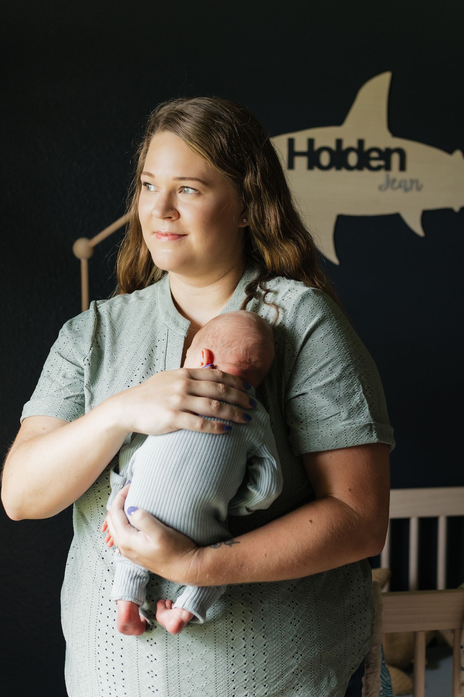 Parent holding sleeping newborn against dark background with nautical nursery decor.