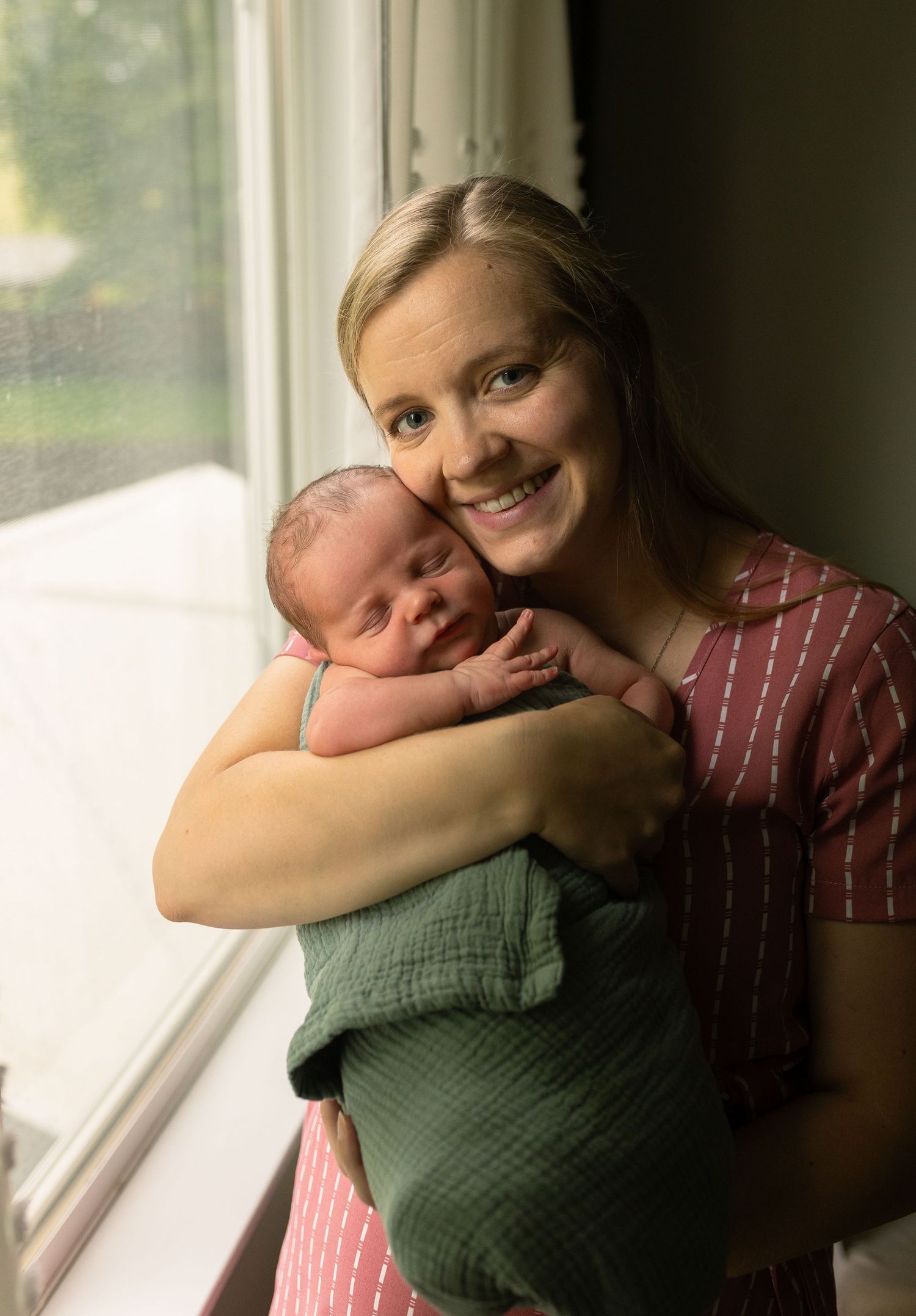 Tender moment between parent and baby by sunlit window.
