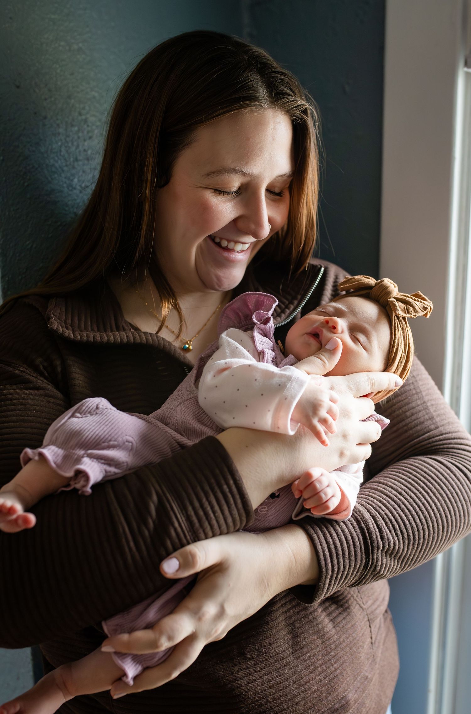 A tender moment captured in warm light as a parent cradles and embraces their baby wearing pink clothing.