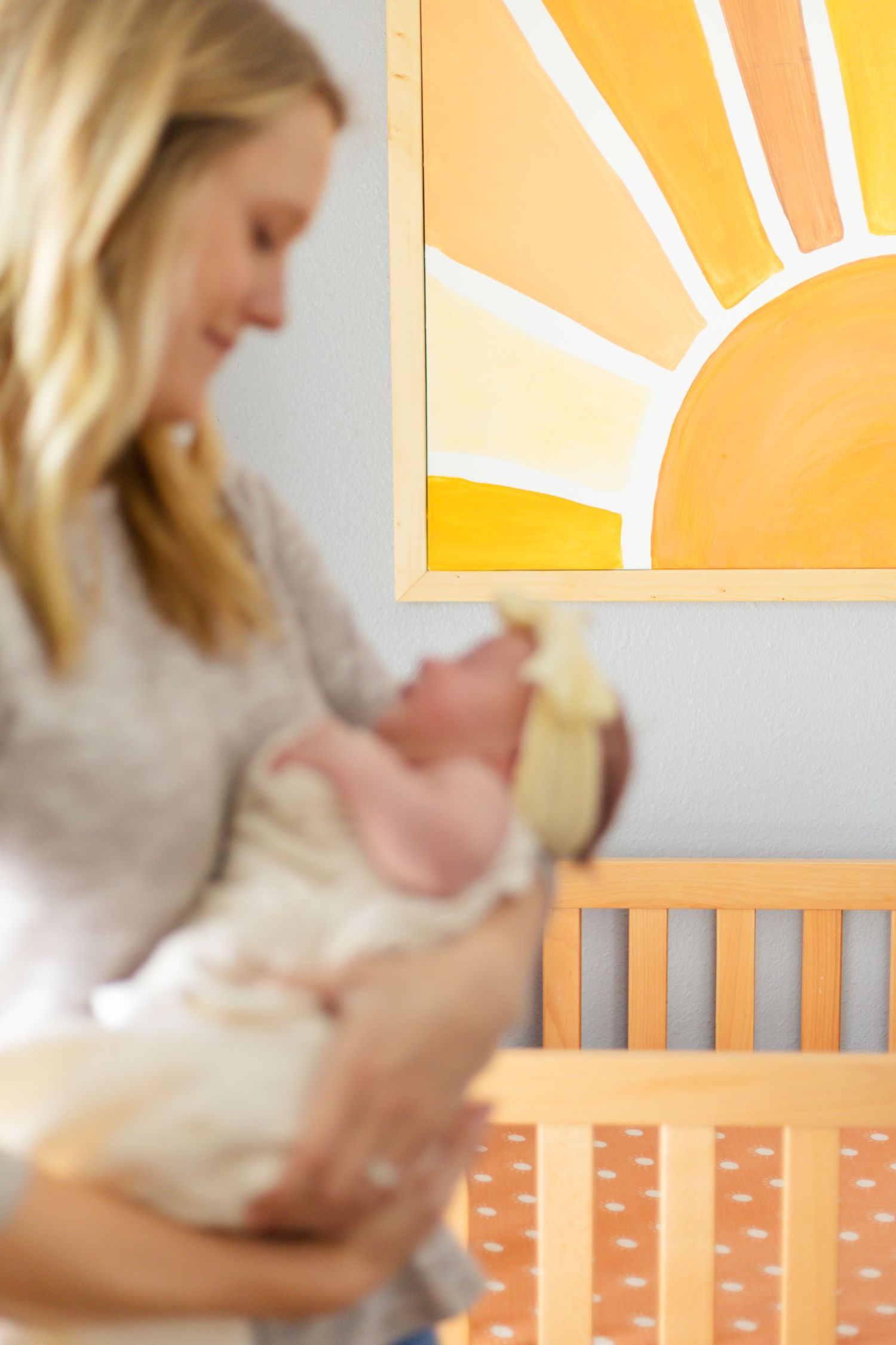 Parent holding newborn in nursery with orange sunburst artwork.