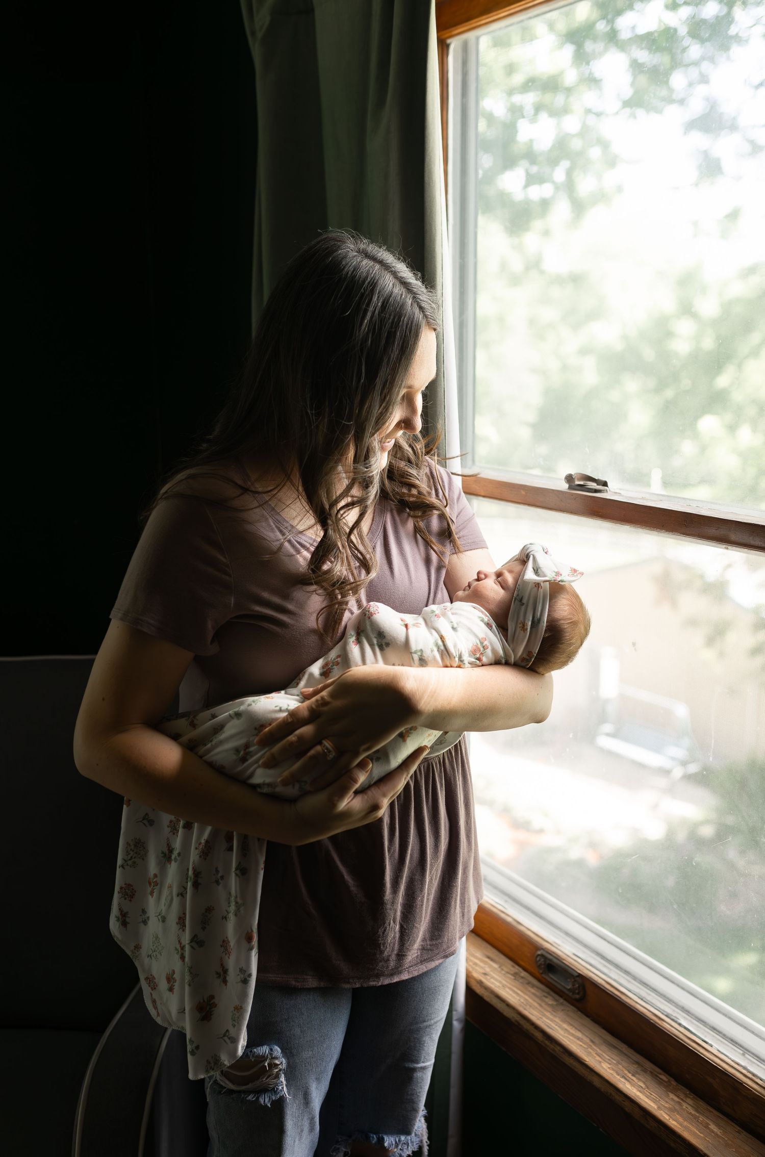 Parent cradling infant by window in soft natural light.