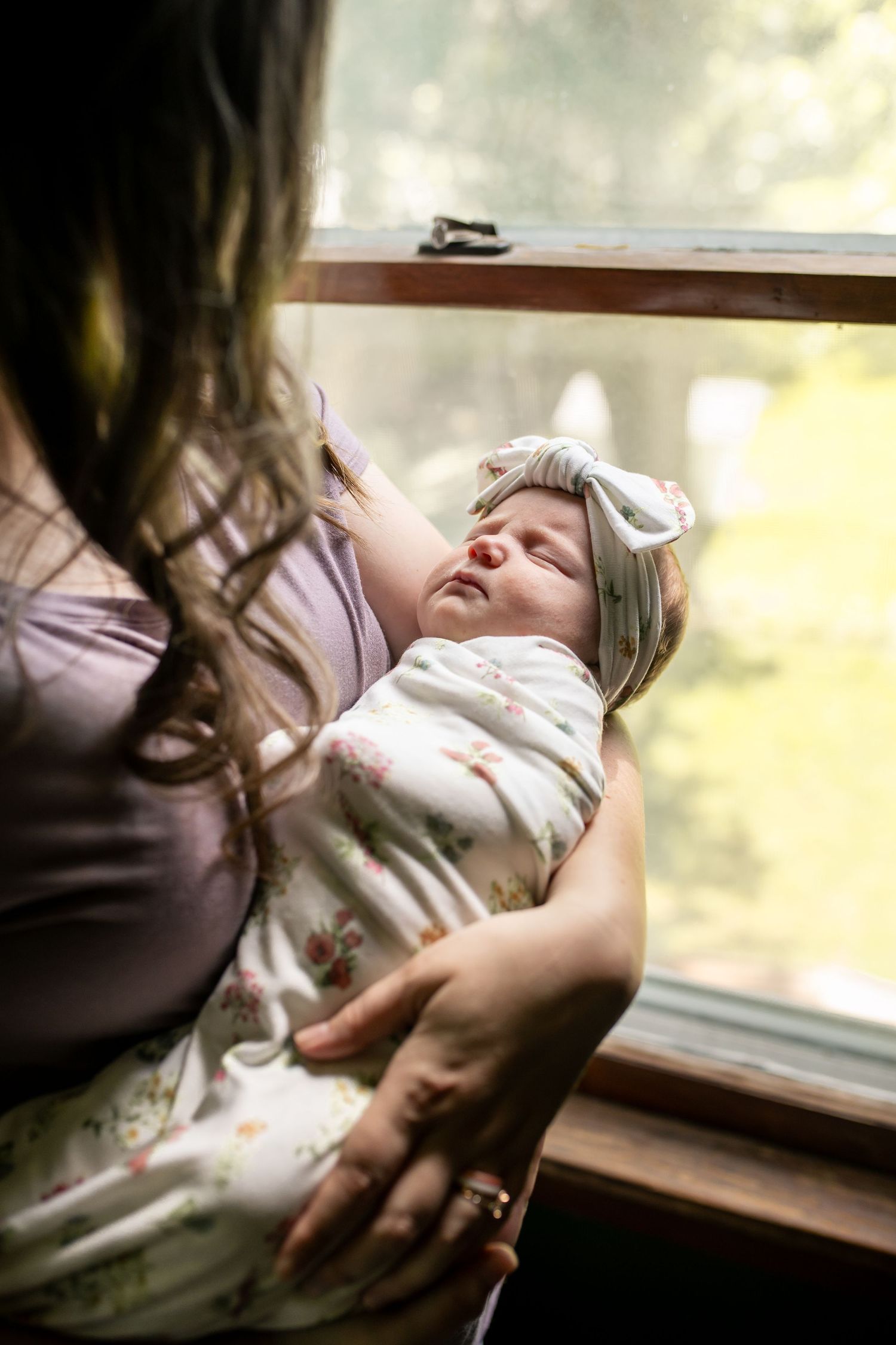 Tender moments between parent and sleeping baby near sunlit window.