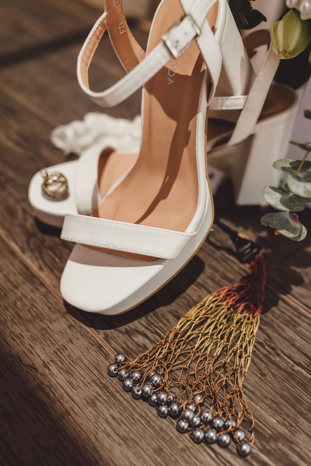 Elegant white bridal shoes and crystal hair pins displayed on rustic wooden surface with decorative elements.