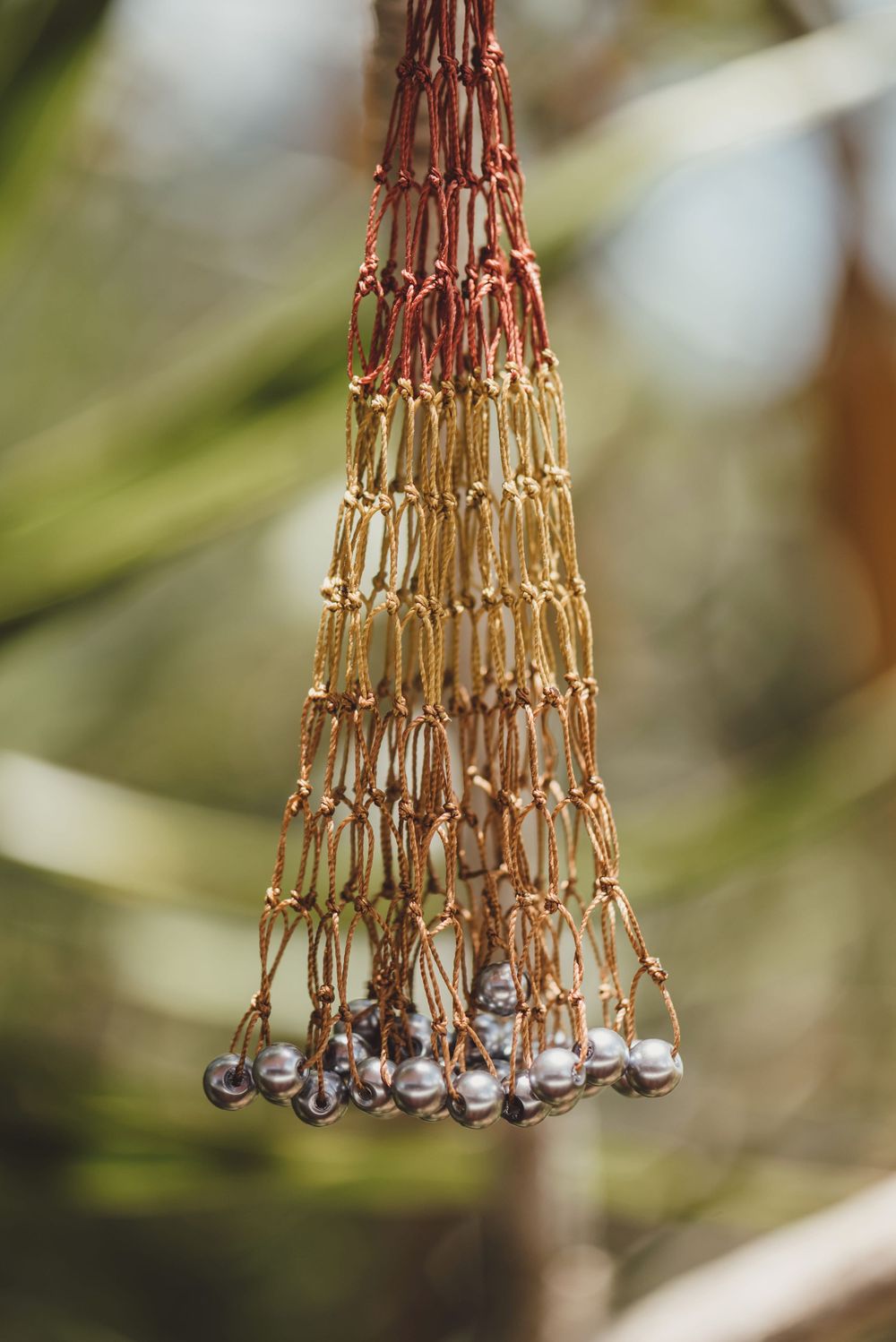 A decorative tapered macrame hanging made of brown and beige cord with small silver beads at the bottom.
