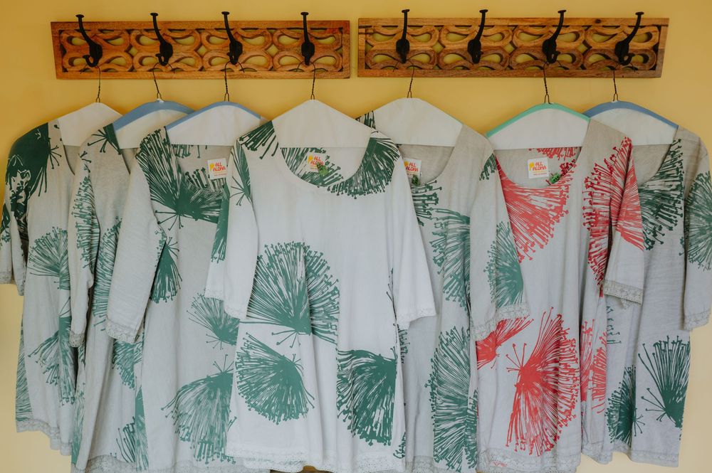 Rows of white t-shirts with green and red artistic prints hanging on a wooden display rack.