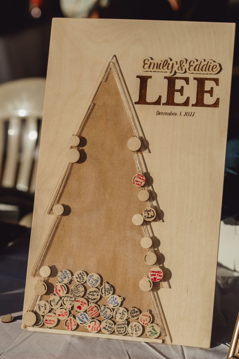 A wooden wedding guest book shaped like a Christmas tree with slots for guests to drop signed wooden discs.