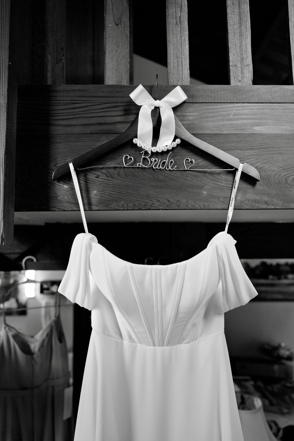 Three white dresses with shoulder straps and bows hanging on wooden hangers in a closet.