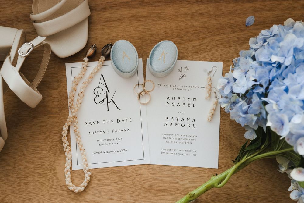 Wedding invitation suite with blue hydrangeas and pearl jewelry displayed on wooden surface.