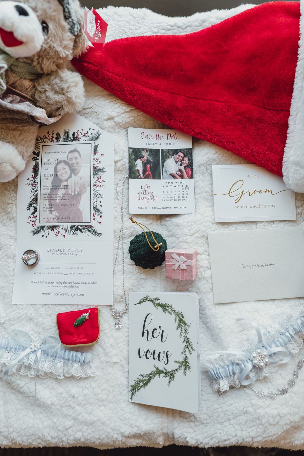 Wedding invitation suite with red dress, stationery, and decor items arranged on white textured background.