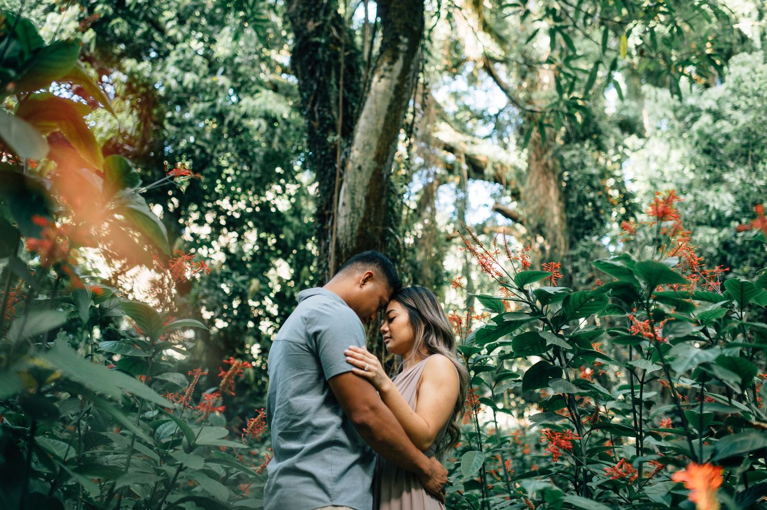 A tender moment captured between two people in a natural outdoor setting with vibrant foliage.