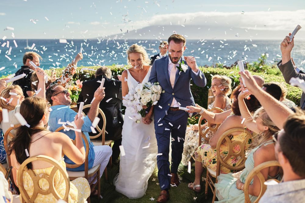 Wedding guests celebrate with confetti toss during an outdoor seaside ceremony.