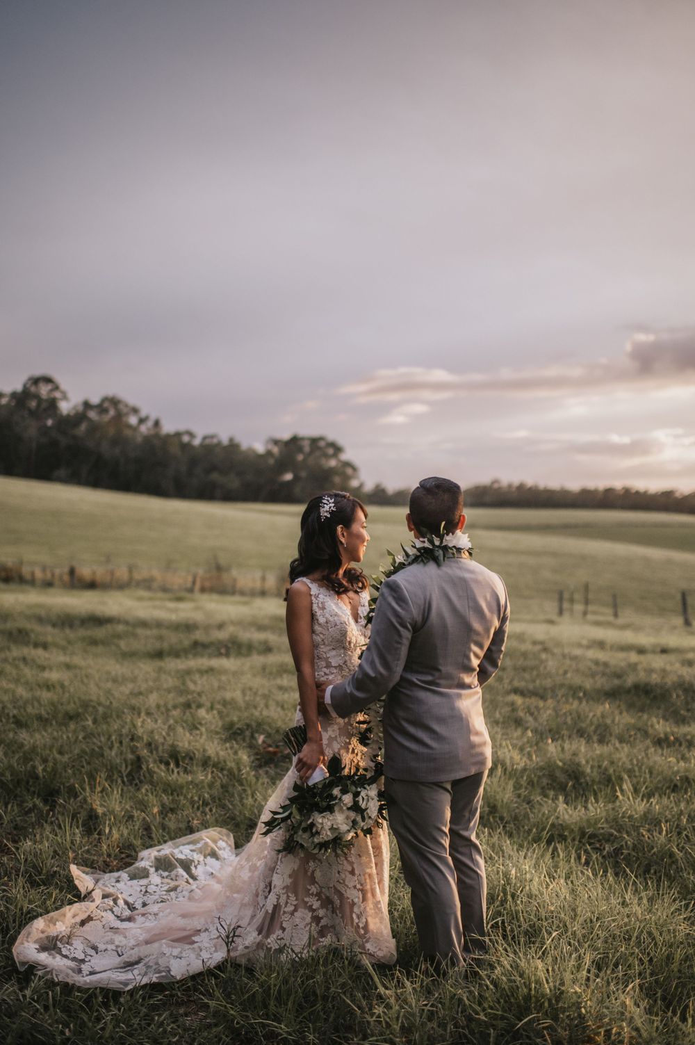 Couple stands together in a scenic field during golden hour sunset.