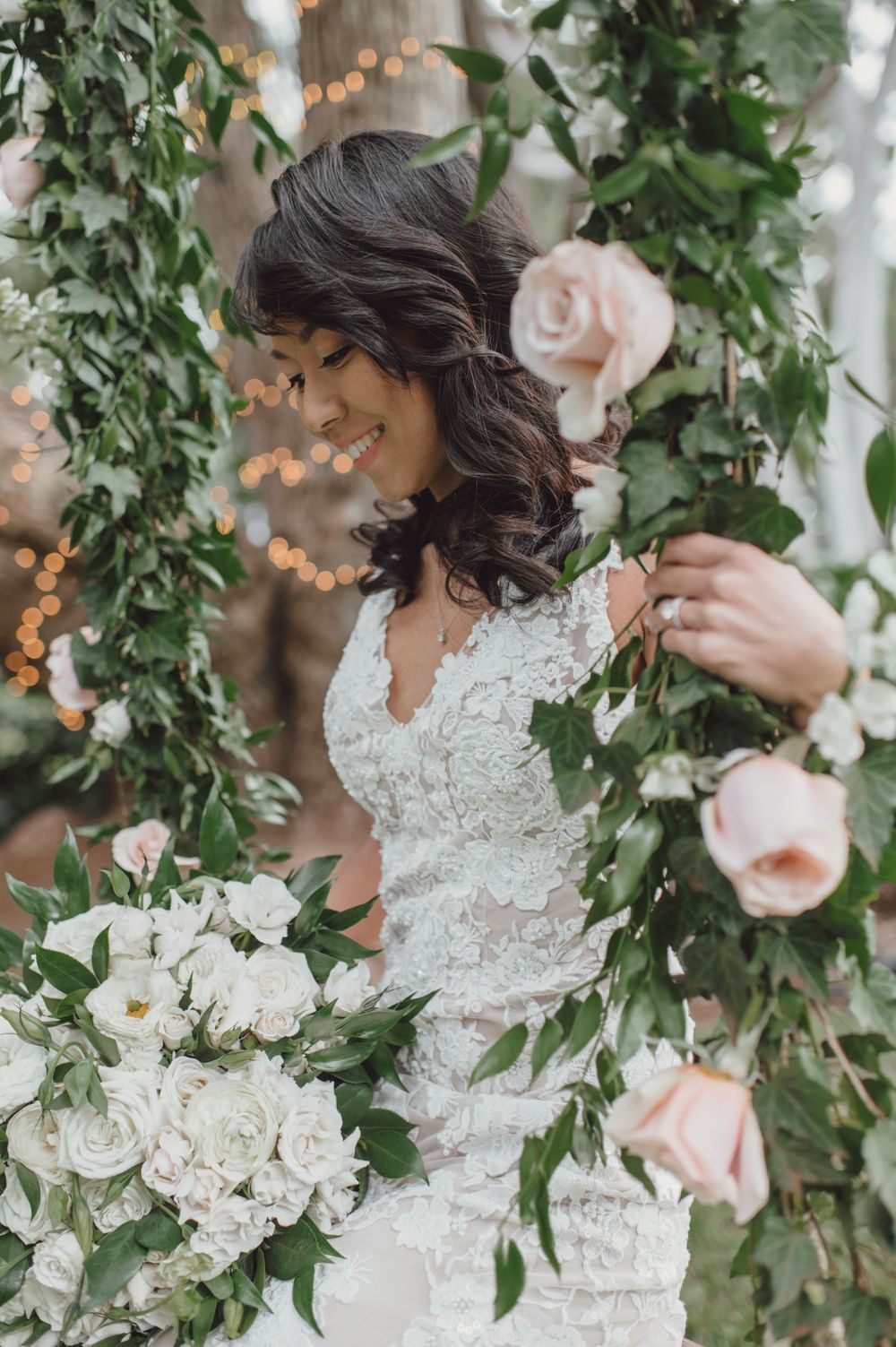 Elegant lace wedding dress detail with cascading greenery and white floral decorations.