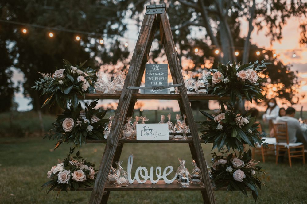Rustic wooden ladder arch decorated with flowers and string lights for outdoor wedding ceremony.