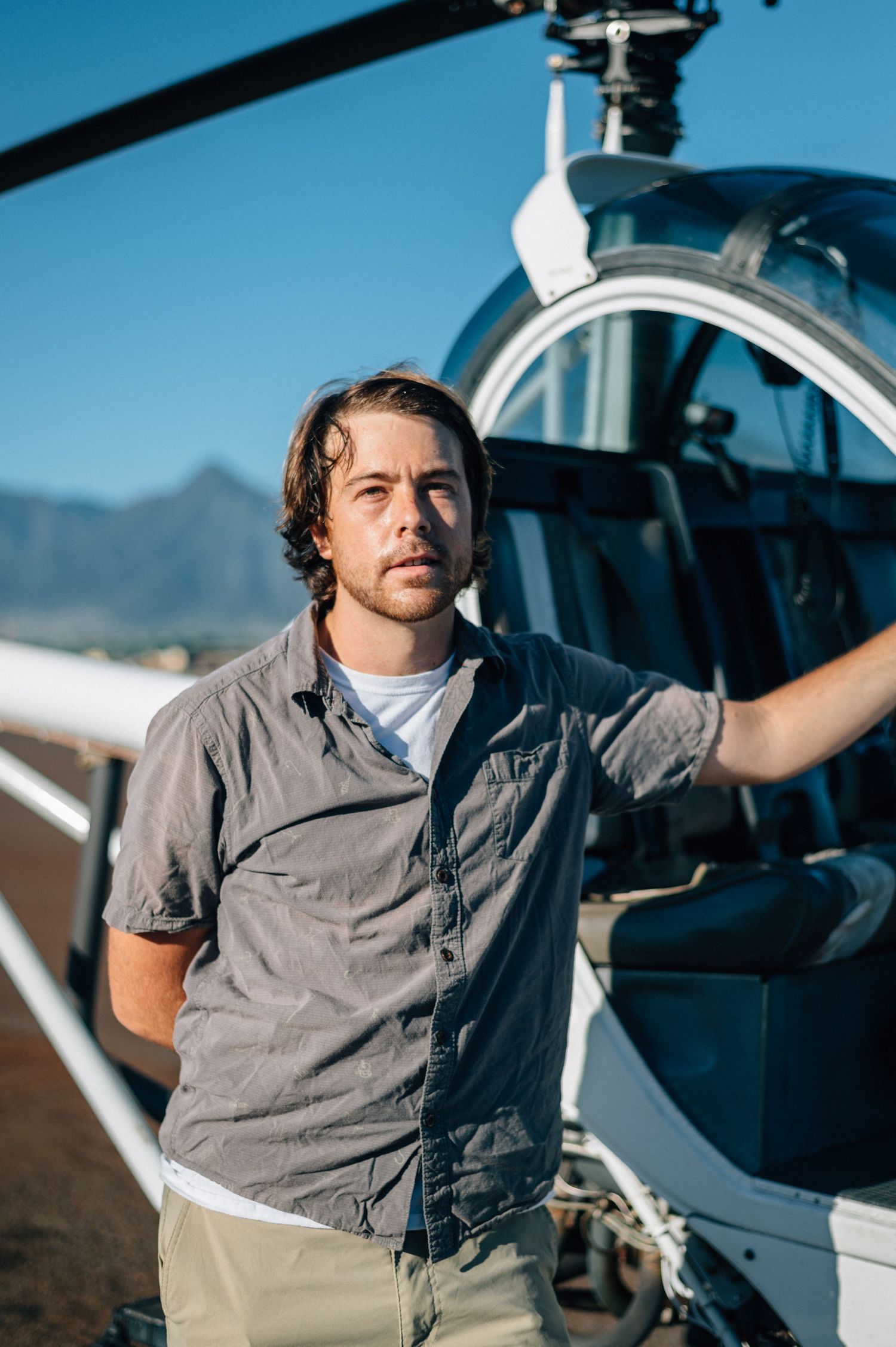Pilot standing next to parked helicopter on desert airfield.