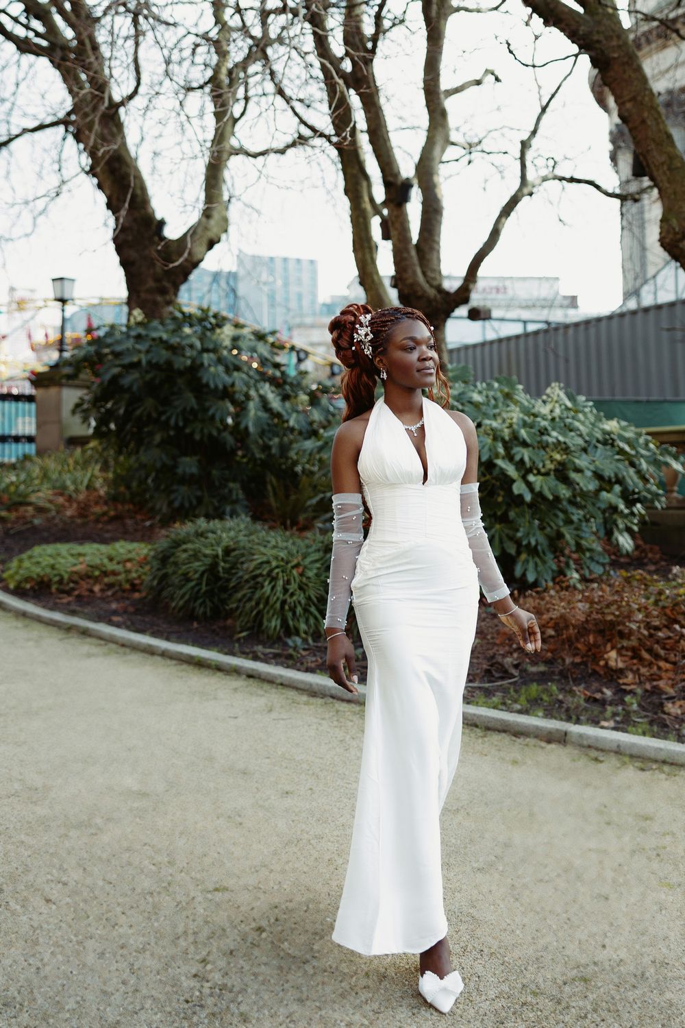 Elegant white halter neck wedding gown with long gloves and a fitted silhouette photographed in an outdoor garden setting.