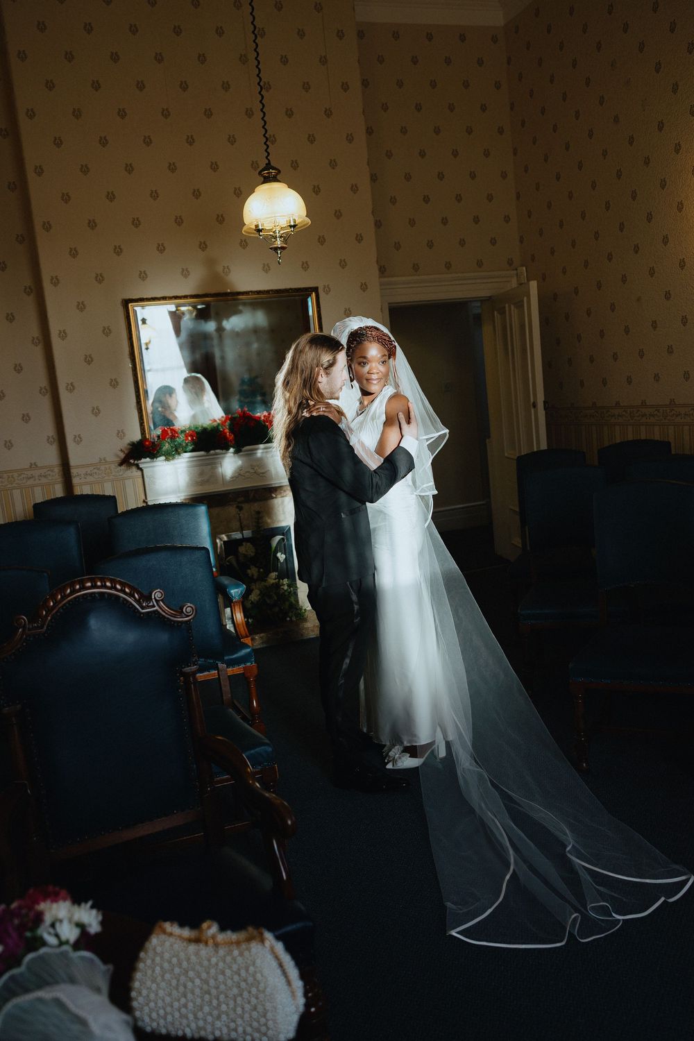 Wedding couple dancing in an elegant room with vintage wallpaper and lighting.