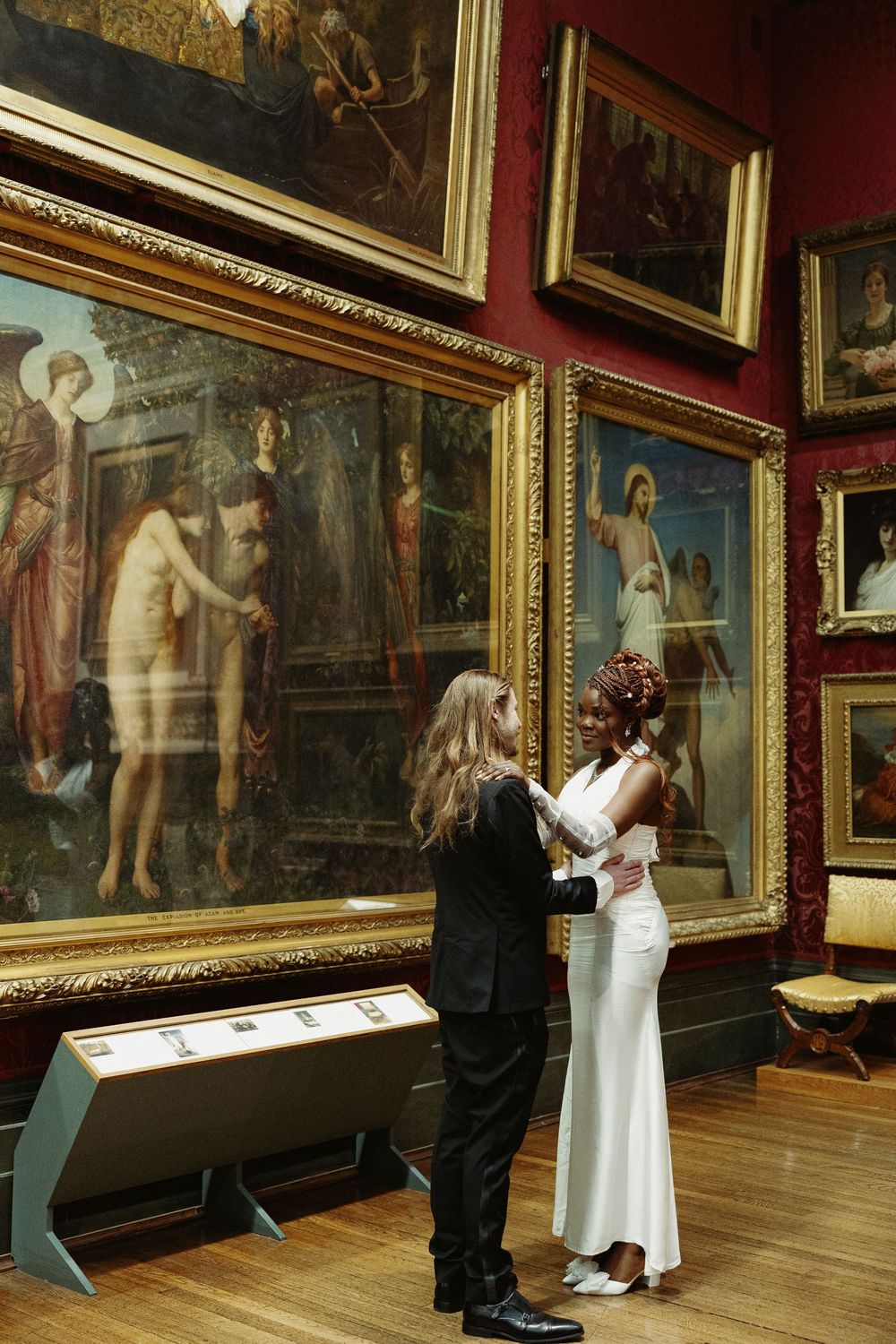 Couple viewing classical paintings in an art gallery with ornate gold frames.