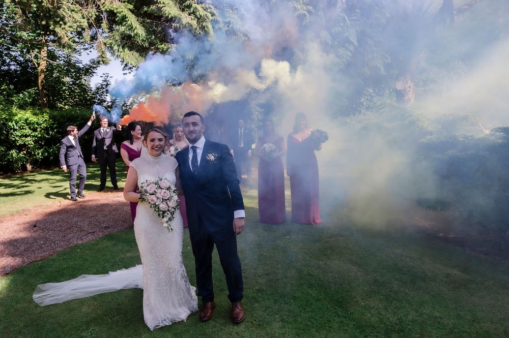 Bride and groom pose with colorful smoke bombs at outdoor wedding ceremony Magheramorne Estate, Co. Antrim