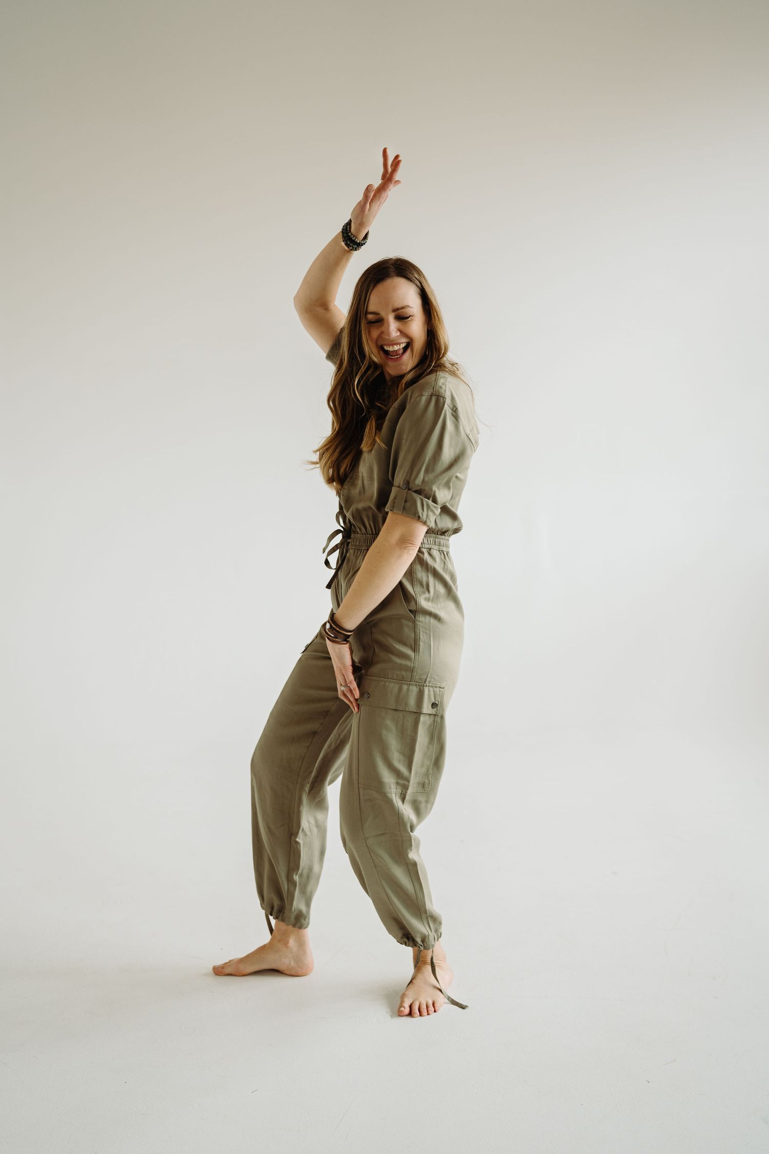 A person in an olive jumpsuit strikes playful poses against a white backdrop in a series of lifestyle photos.
