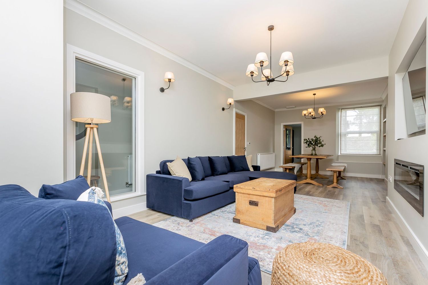 Modern living room with navy blue sofas, wooden chest coffee table, and tripod floor lamp on light hardwood floors.