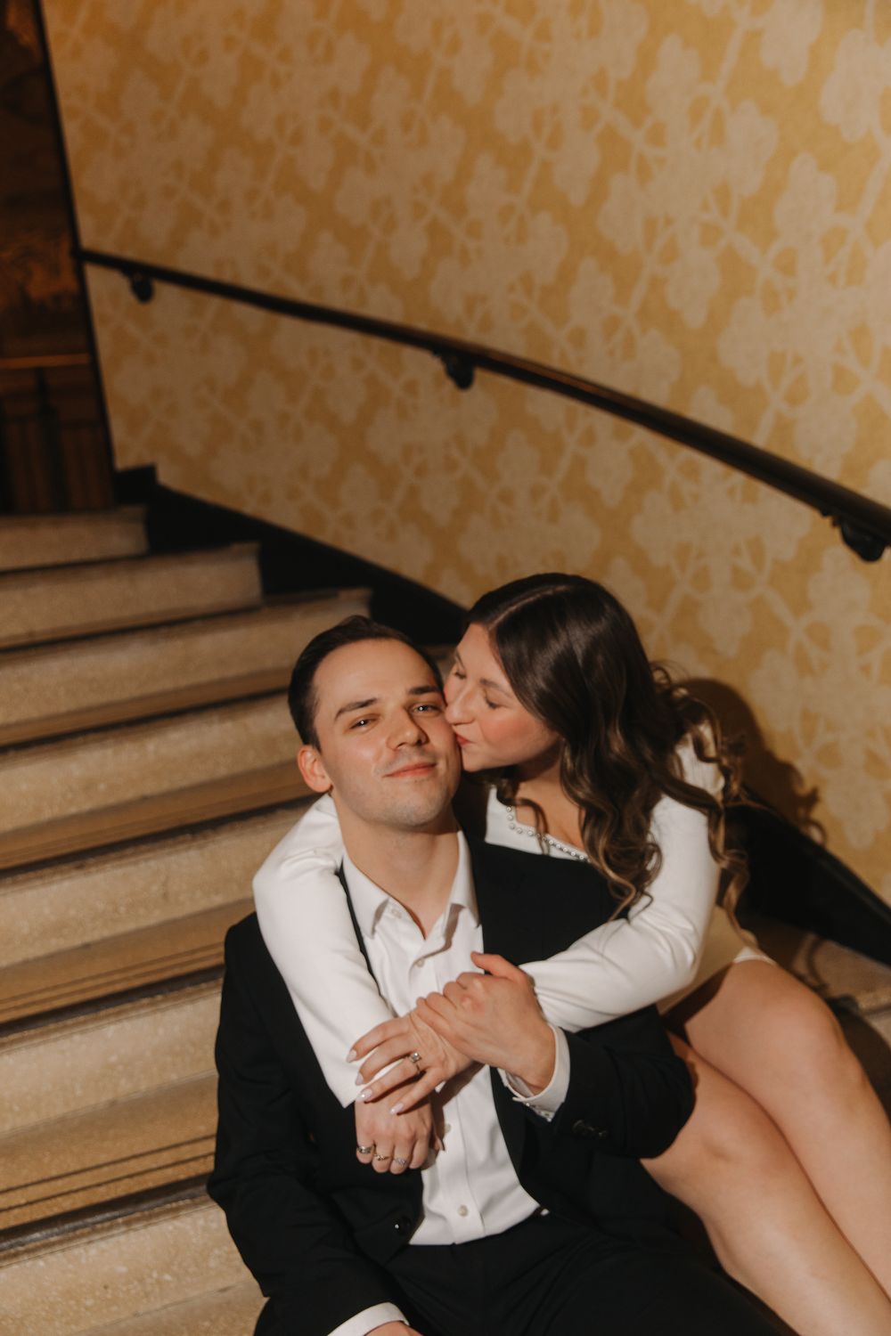 A couple shares an intimate moment while sitting together on carpeted stairs.