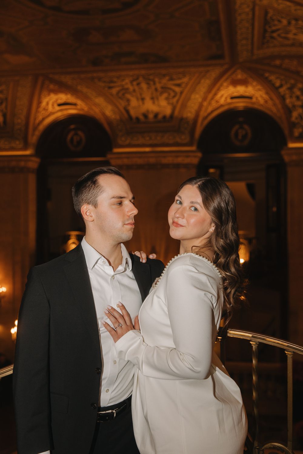 A romantic couple shares intimate moments in an elegant candlelit ballroom with ornate decor and warm lighting.