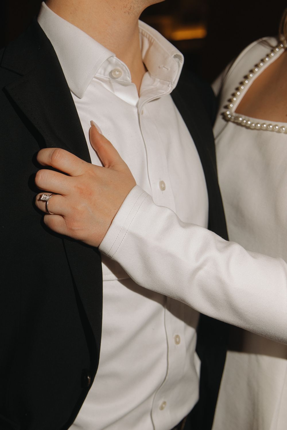Close-up view of white dress shirt sleeves and collar details against a dark background.