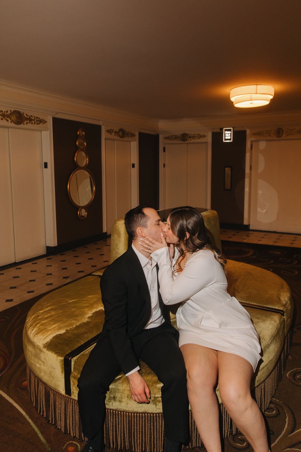 A couple shares an intimate moment on a gold velvet couch in a dimly lit room.