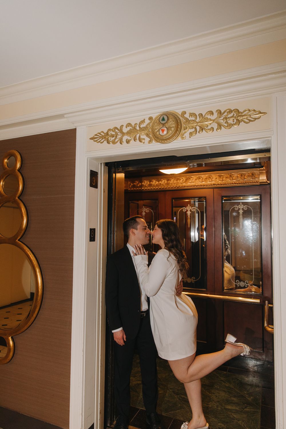 A couple in formal attire shares a romantic dance move in a hotel hallway with ornate gold decor.