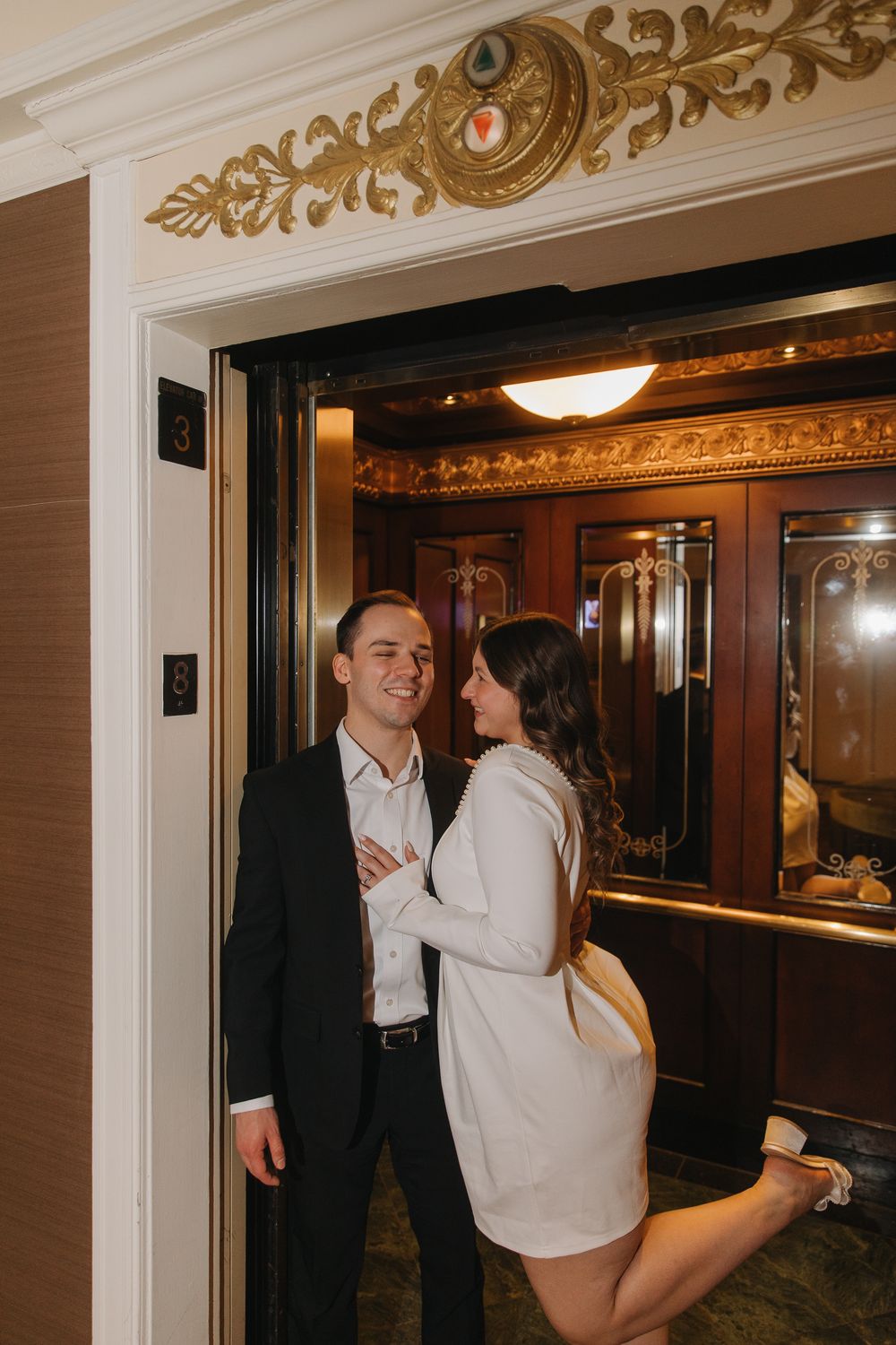 Couple sharing a romantic moment in an elegant hallway with ornate gold trim and mirrored walls.