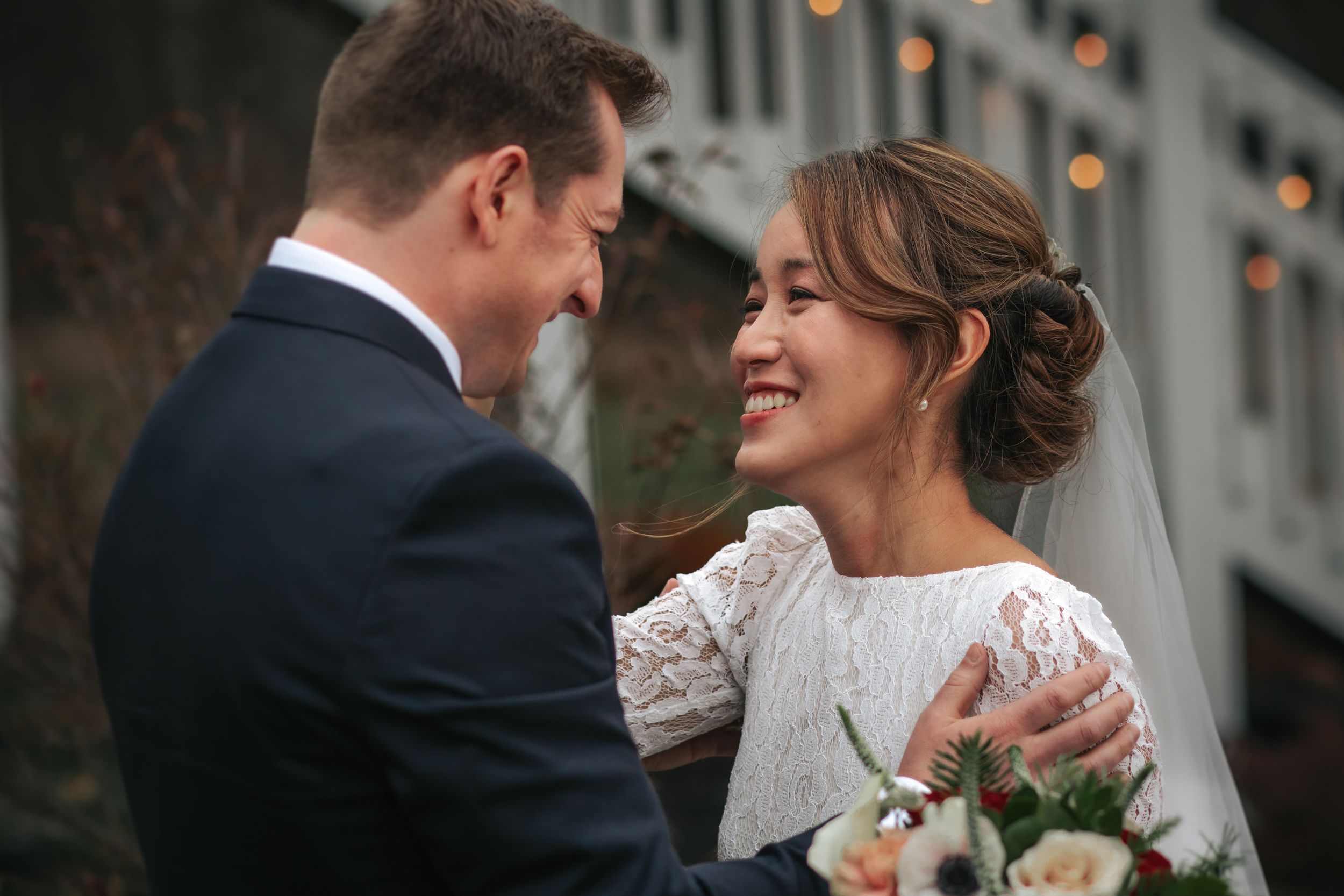 A joyful wedding moment captured between newlyweds with the bride in a lace dress holding a bouquet.